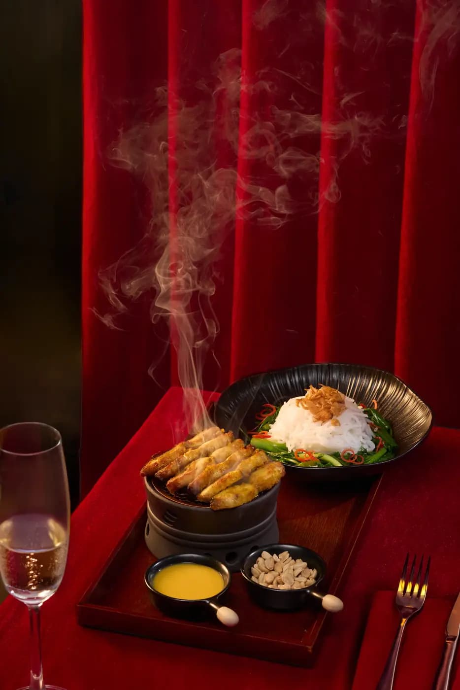 A steaming tray of dishes and a glass of wine on a red table, Moulin de Da Nang