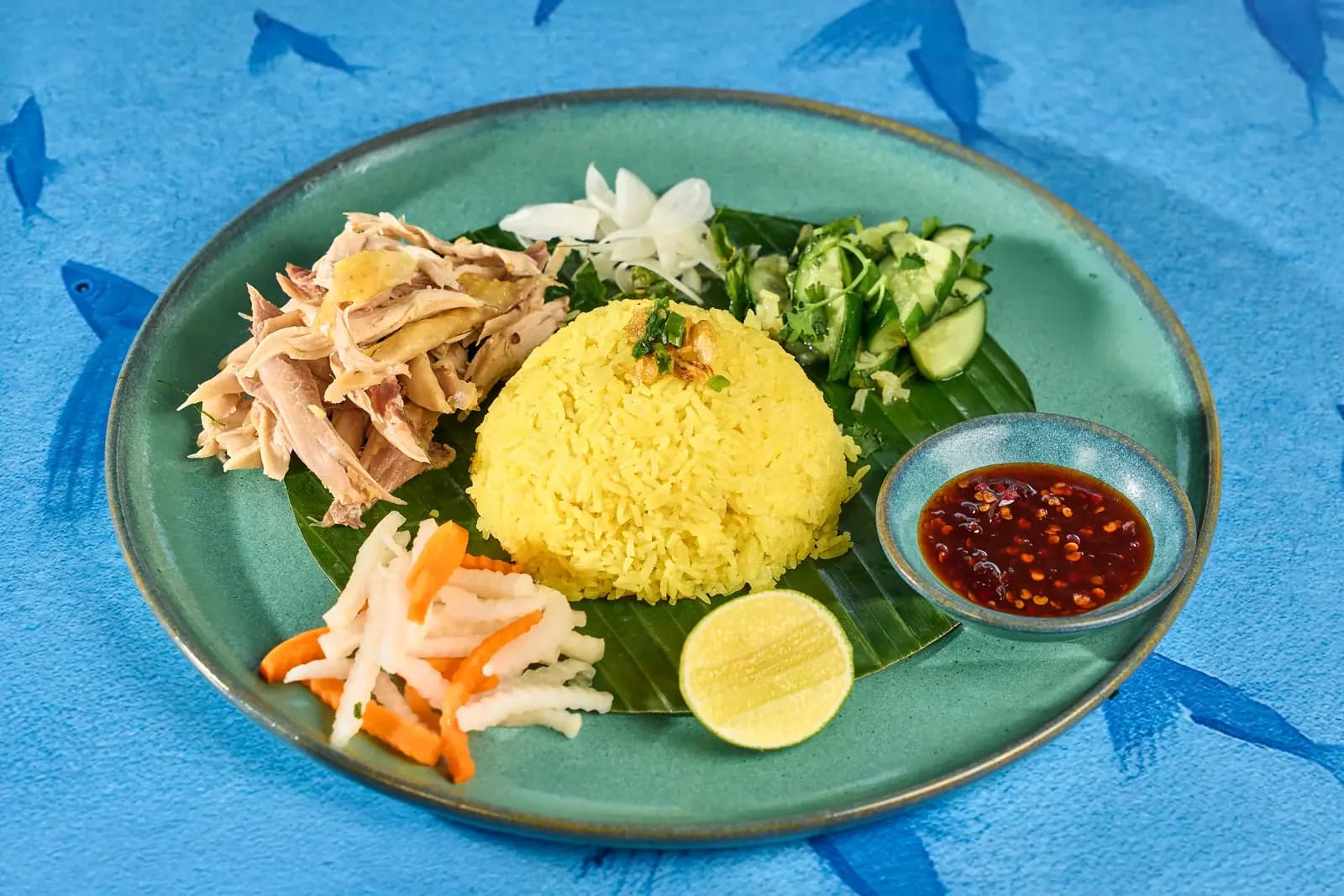 Turmeric chicken rice on a teal plate against blue, Premiere Village