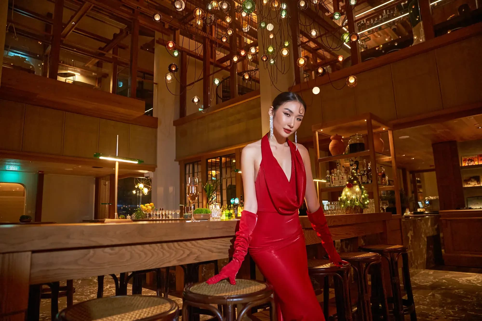 A model in a red gown at a warmly lit bar, XITA x Hoiana fashion shoot