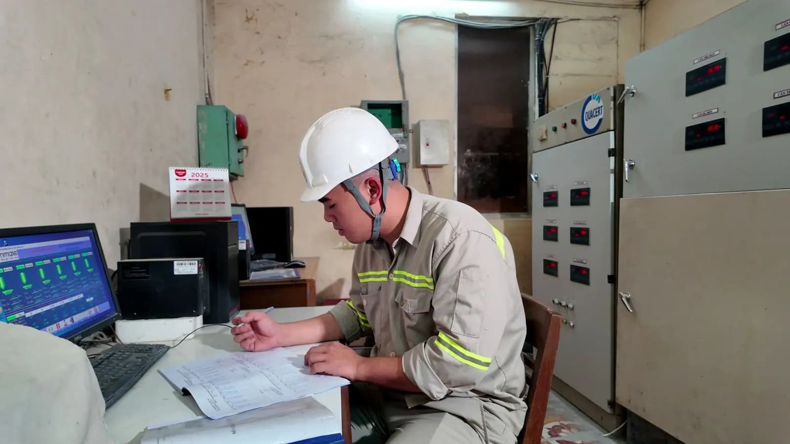 Vận hành viên đội mũ bảo hộ theo dõi hệ thống trong phòng điều khiển